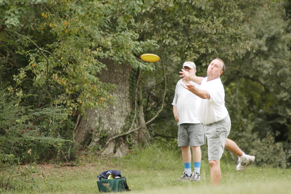 Two men playing disc golf; one throwing a disc