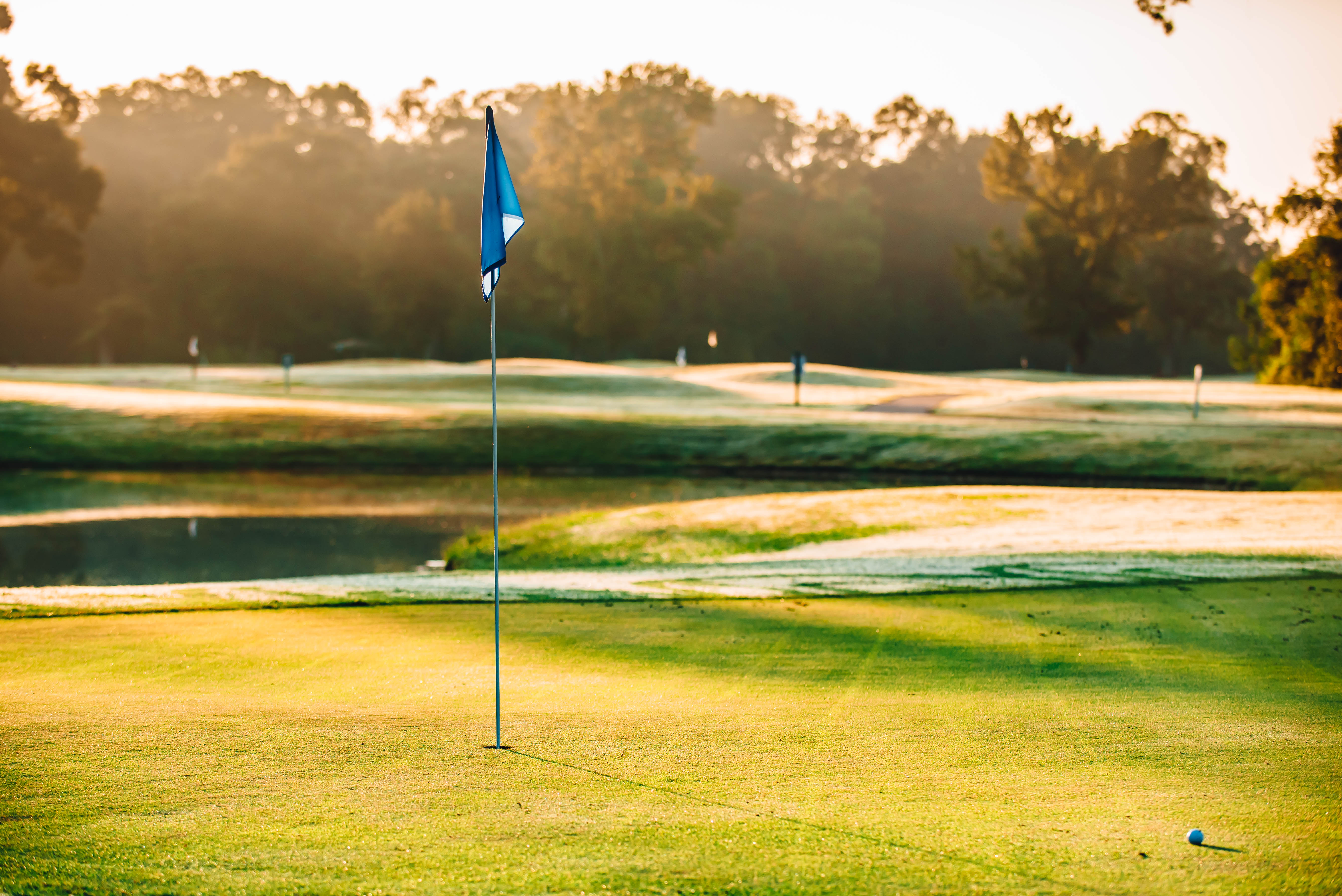 Photo of golf course with blue flag and sunset