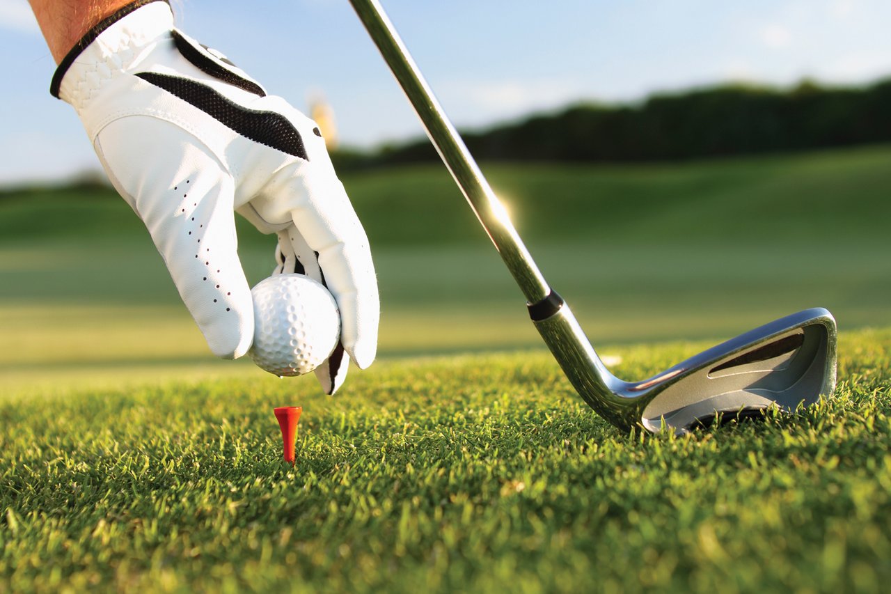 hand with glove glove placing golf tee on course