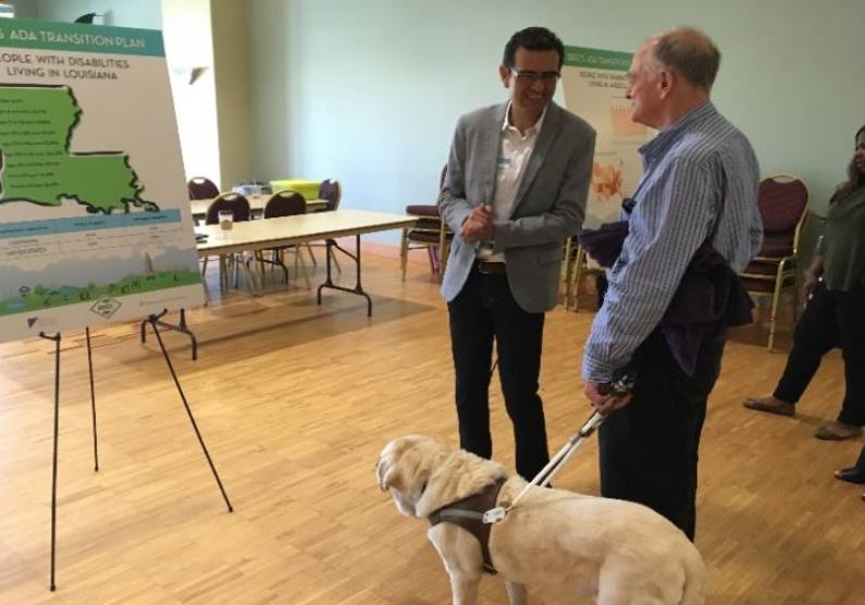 People talking in front of display board, of them is man holding leash of service dog