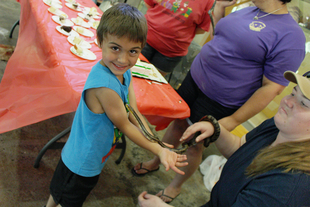 Boy with snake crawling up arm, smiling at camera 