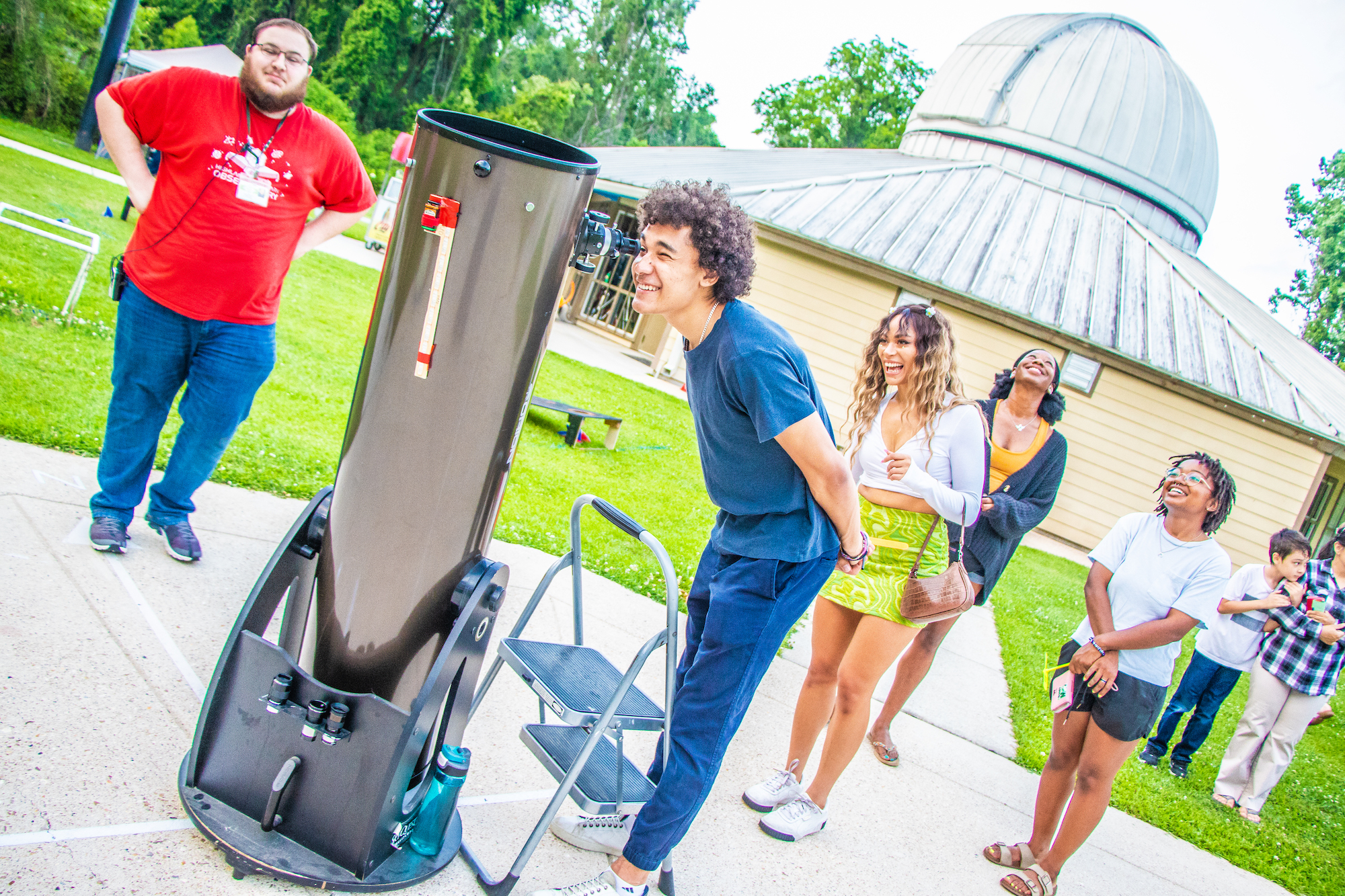 Photo of man looking through telescope as a group of people watch